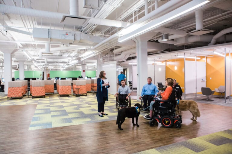 Des personnes en fauteuil roulant avec des chiens guides visitent l'intérieur d'un bâtiment accessible.